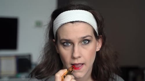 Young woman applying lipstick at home 4K