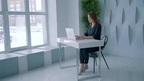 Beautiful Woman is Sitting at Desk in Office Action Businesswoman is Typing on Laptop in Stylish