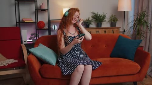 Happy Relaxed Girl in Wireless Headphones Dancing Listening Favorite Rock n Roll Music on Home Couch