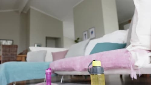 Close up of water bottles, towels and yoga mats on floor of living room, slow motion