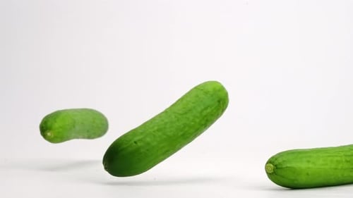 Whole Persian mini cucumbers bouncing onto white table top and rolling around in slow motion