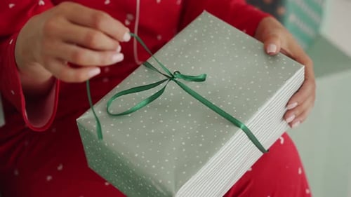 Person unwrapping green ribbon on Christmas gift