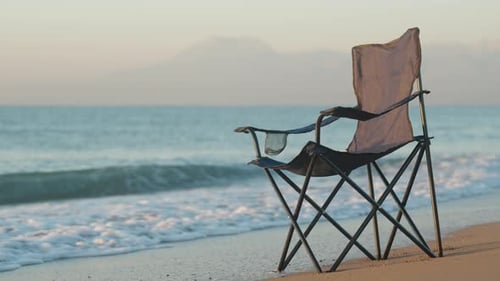 Folding Blue chair by the sea. We meet the dawn on the sandy beach, The Mountains are Behind. Slow m