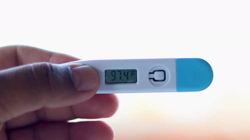 Ill man holds digital thermometer with body temperature reading in Fahrenheit up close to the camera