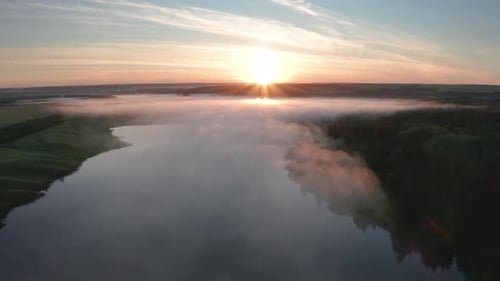Aerial view of the summer fog forming over the lake during sunrise
