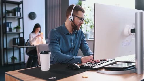 Online-Treffen, Reden. Ein Mann mit Kopfhörern mit Mikrofon arbeitet an einem Computer im Büro.
W