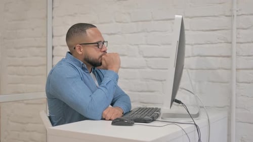 Nachdenklicher gemischtrassiger Mann denkt bei der Arbeit am Computer