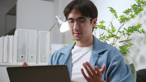 Young caucasian man working remote in home office, using laptop computer during video call meeting.