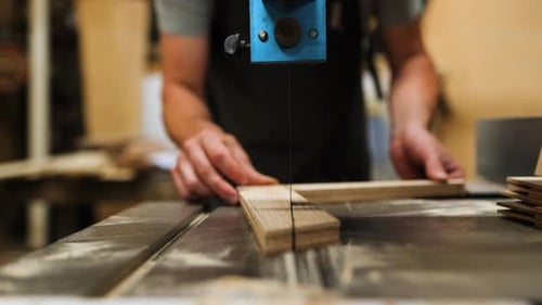 Craftsman operates a band saw in a woodworking shop to create precise cuts on wooden planks during t