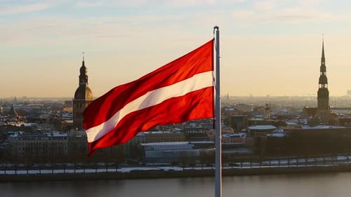 Latvian Flag Waving Over Cityscape on Sunny Day