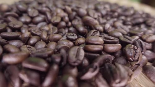 Close-up of roasted coffee beans falling one by one and piling up