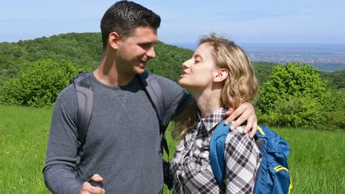 Young couple enjoying hiking together in nature standing on the top of the hill.