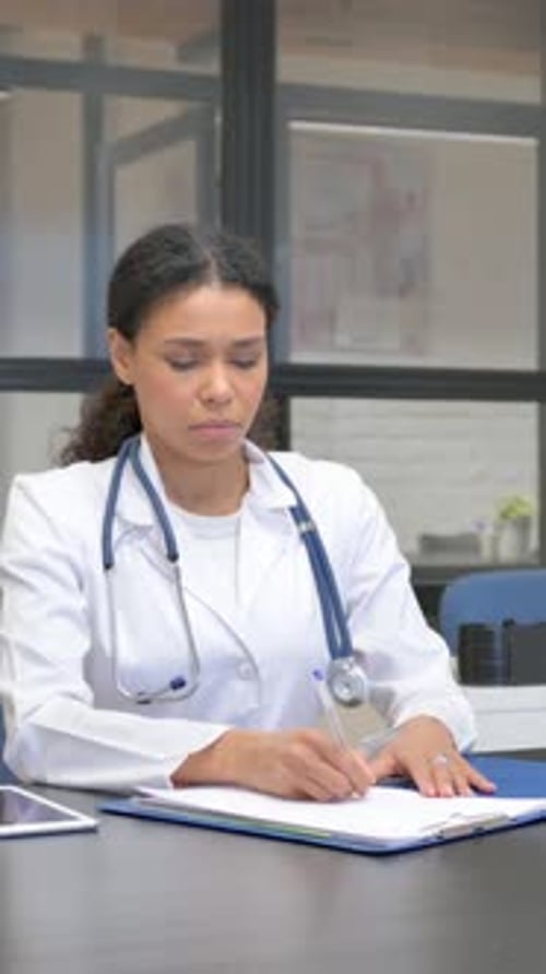 African Female Doctor Writing Medical Report in Hospital, vertical video