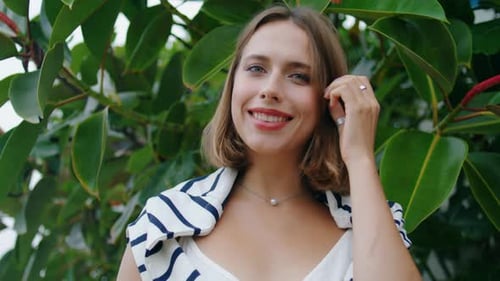 Attractive Woman Posing Park at Green Leaves Closeup. Girl Adjusting Hair Looking