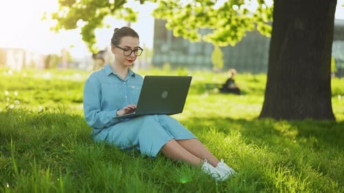 Busy Attractive Woman Working on the Laptop As Sitting on Grass in City Park