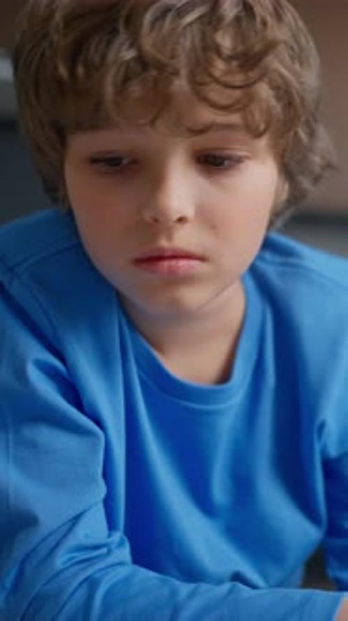 Young Boy in a Blue Shirt Concentrating Quietly While Drawing with a Colorful Marker at a Table