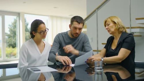 Sitting at the Table in the Living Room Real Estate Agent and Beautiful Young Couple Sign Documents
