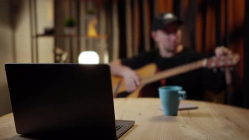 Man Plays Guitar with Laptop at Home