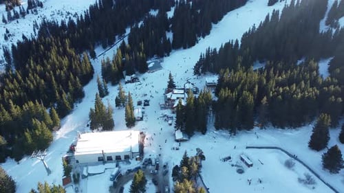 Overhead aerial clip of a busy mountain ski resort with skiers and snowboarders on a slope and a cab
