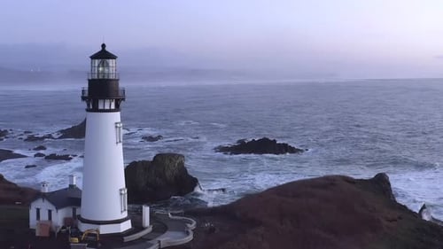 Aerial forward toward Yaquina Lighthouse and waves breaking on rocks. Oregon