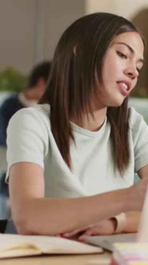 Vertical video: Reacting to cue, mint tee woman taking notes, gesturing at laptop in study area