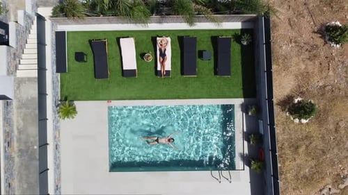 Drone flying over an outdoor pool in bird's eye view - Woman in swimming costume lying on sunbed and