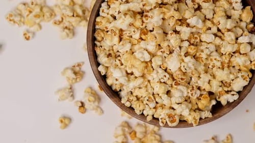 Popcorn Tossed in a Wooden Bowl on a White Background Slow Motion Video Close Up Top View