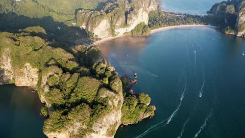 Drohnenaufnahme von Booten, die sich über türkisfarbenes Wasser in der Nähe dramatisch Kalksteinfelsen und des Strandes in