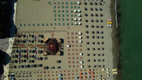 Beach with umbrellas and sun loungers in a row on the sand kissed by the Adriatic Sea, tourists sunb