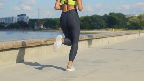 Athletic Woman Jogging Along Sunny Waterfront Listening to Music