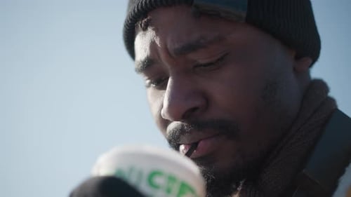 Photographer Sipping Coffee Holding Camera Strap on Snowy Urban Street Winter Daylight