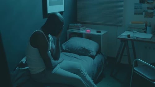 Bald Man Sitting on Bed in Dim Room