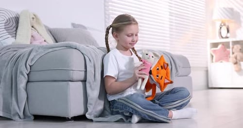 Cute girl playing with puppets on sofa at home