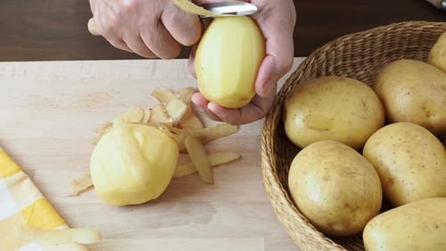 Hands peeling potatoes on a wooden board