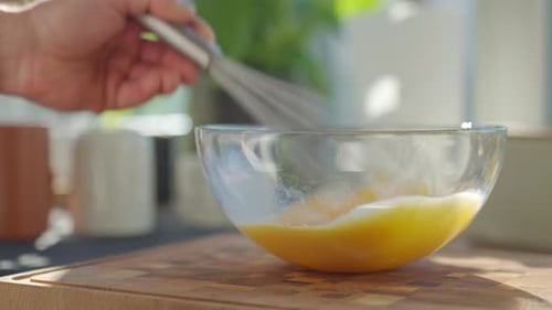 Eier in Glasschale auf Holzbrett mit den Händen verquirlen