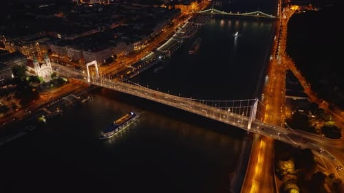 Aerial View of Traffic on Illuminated Erzsebet Bridge in City Centre at Night Boats Passing on Wide