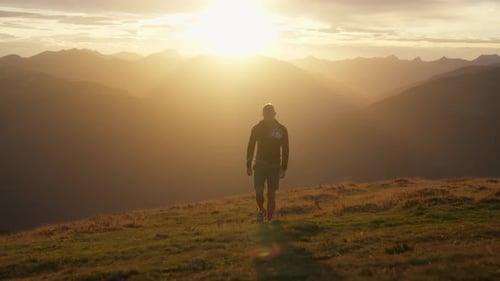 Man Walking Toward Mountain Sunset on Grassy Hill