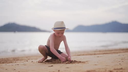 Boy With A Hat Digging Up Sand At The Beach