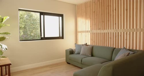 Sonniges Wohnzimmer mit grünem Sofa und Holzwand, das eine gemütliche Atmosphäre schafft, Kopierraum