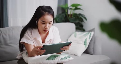 Junge Frau mit Kopfhörern und Tablet-Technologie, die sich zu Hause auf dem Sofa entspannt.
