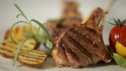 Grilled lamb chops with rosemary, focus on meat with blurred vegetables in background, high-end cuis