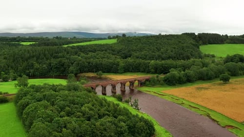 Aerial dolly shot of the English countryside showing a viaduct spanning over a flowing river, bright