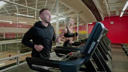 Man and Woman Running on Treadmills in Gym