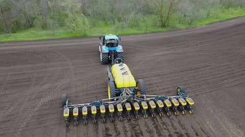 Blue tractor with yellow seeder working on the field in Ukraine OA