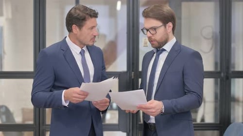Businessmen Discussing Documents while Standing in Office
