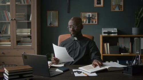 Focused Cleric Reads at Desk Indoors