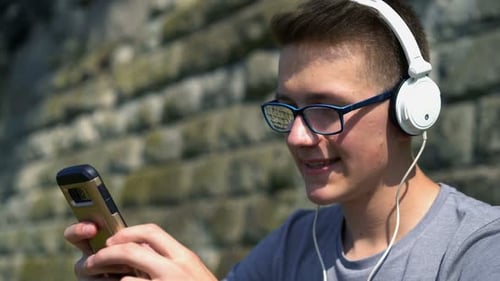 Teenage boy enjoying music on smartphone and relaxing in the city park on a sunny day