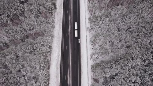 Top View of Lonely White Car on Highway Surrounded By Winter Forest and It is Overtaken By Truck