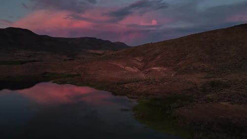 Aerial Sideways movement of the sunsets pink reflection off clouds, with pond reflections