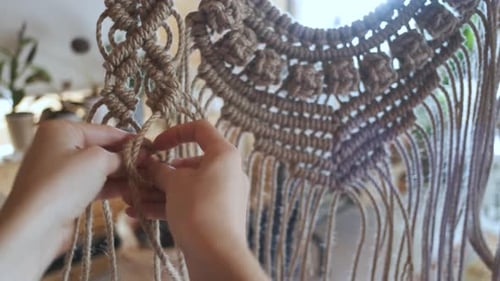 close-up of female hands weaving macrame from a rope